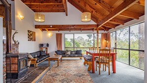 Una sala de estar acogedora con chimenea, muebles de madera y ventanas amplias que dan a un paisaje exterior.