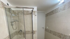 Uma casa de banho com chuveiro separado por vidro, sanita e azulejos estampados nas paredes e no chão.