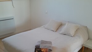 En snyggt bäddad säng med ett beige täcke och kuddar, en låda med toalettartiklar och ett trägolv.
