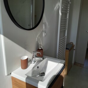 Un baño con un lavabo blanco, un espejo redondo, un dispensador de jabón y una taza.