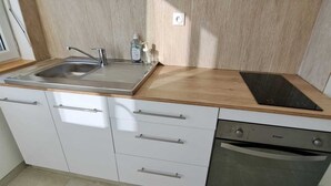 Ett modernt kök med en diskho i rostfritt stål, en bänkskiva i trä, vita skåp och en inbyggd diskmaskin.
