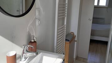 Une salle de bain avec un lavabo blanc, un miroir, un porte-serviettes et un espace douche.