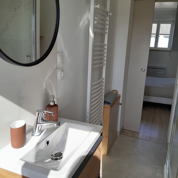 Un baño con lavamanos blanco, un espejo, toallero y zona de ducha.