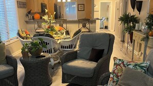 A cozy living room with wicker furniture, a dining table with a centerpiece, and a kitchen in the background. - Beautiful Lakeside Condo/The Maples Golf Course On Site/Golf Haven/Near Pinehurst & Southern Pines/40 Golf courses minutes awaySleeps 9 (Vass)