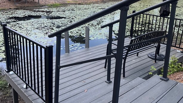 A wooden deck with a railing overlooking a pond with lily pads, surrounded by trees and a row of buildings with a uniform architectural style. - Beautiful Lakeside Condo/The Maples Golf Course On Site/Golf Haven/Near Pinehurst & Southern Pines/40 Golf courses minutes awaySleeps 9 (Vass)