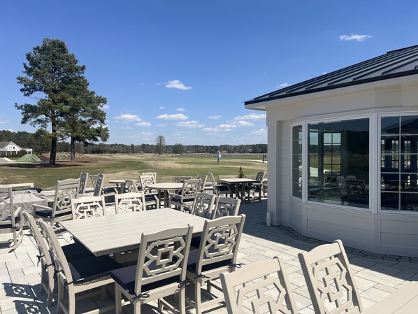 Un patio al aire libre con mesas y sillas, una zona de estar cubierta y vistas a un campo de golf.