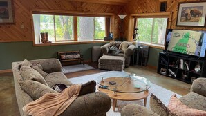 A cozy living room with a wooden ceiling, large windows, a glass coffee table, and a television. - Four Season Private Retreat (Hager City)