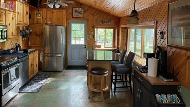 A cabin kitchen with wooden walls, a stainless steel refrigerator, a stove, and a dining area with two chairs. - Four Season Private Retreat (Hager City)