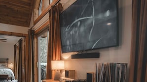 Une chambre moderne dotée d’un grand téléviseur à écran plat fixé au mur, d’un parquet, d’une commode en bois et d’une grande fenêtre avec des rideaux.