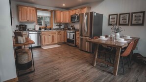 Une cuisine moderne avec des meubles en bois, des appareils électroménagers en acier inoxydable et un coin repas comprenant une table et des chaises en bois.