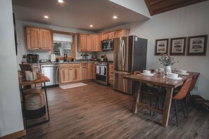 A modern kitchen with wooden cabinets, stainless steel appliances, and a dining area with a wooden table and chairs.