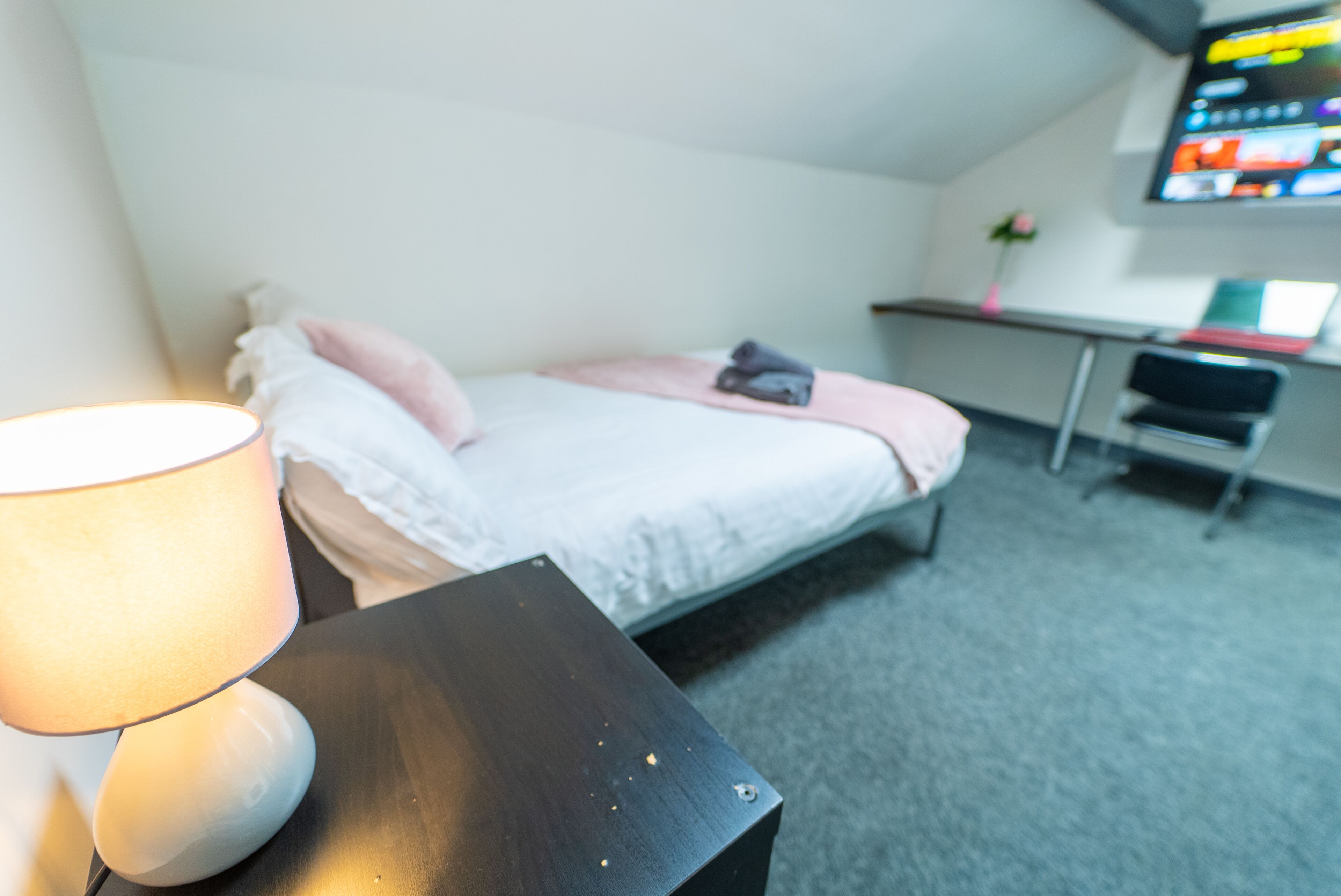 A hotel room with a bed, a desk, a chair, and a TV on the wall.