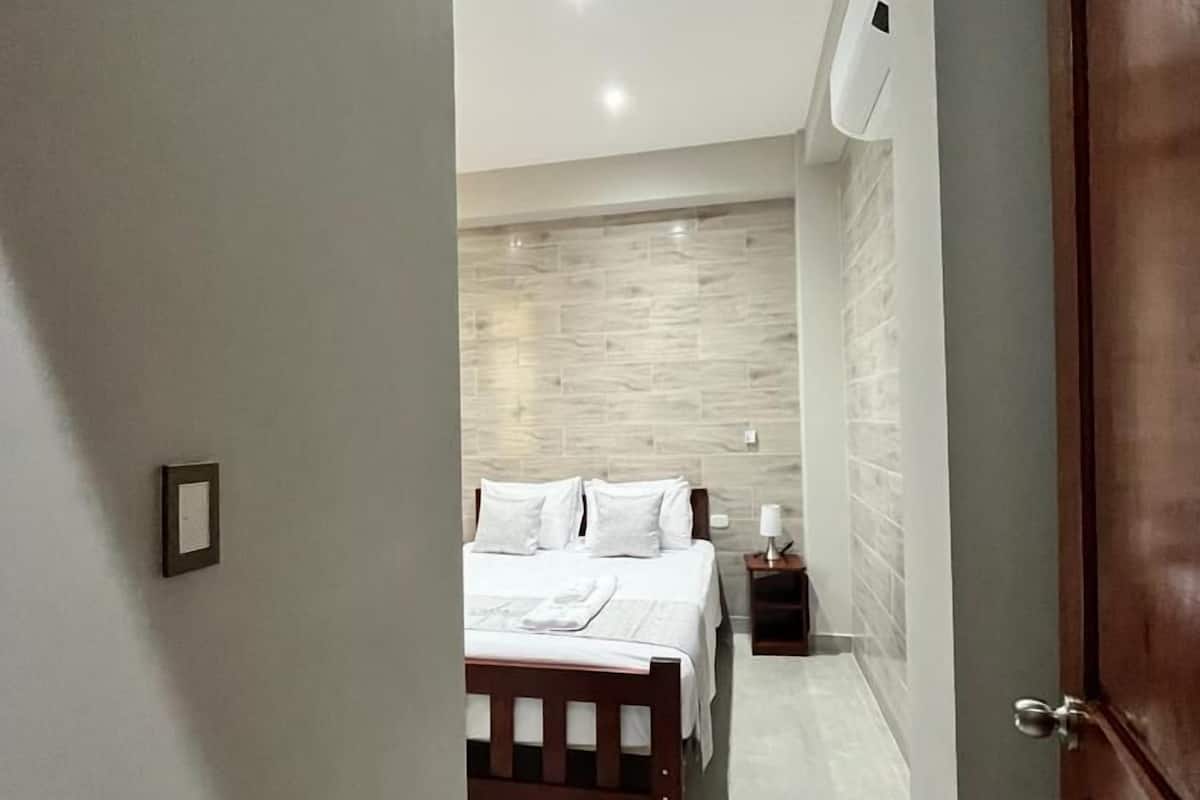 Ein modernes Hotelzimmer mit einem hölzernen Bett, einem Nachttisch und einer Wand-Klimaanlage.