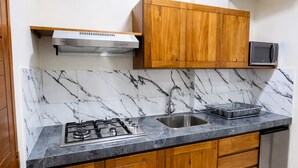 A kitchen with wooden cabinets, a gas stove, a microwave, and a stainless steel sink. - Bellazio Aparthotel (Iquitos)