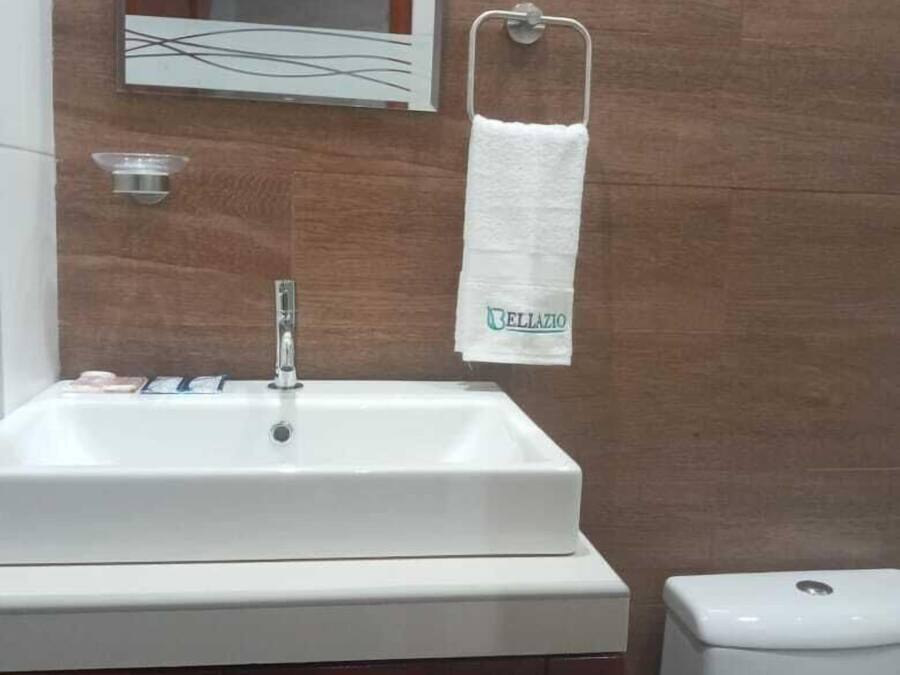 Un baño con un lavabo blanco, un espejo y una toalla colgada en un perchero.