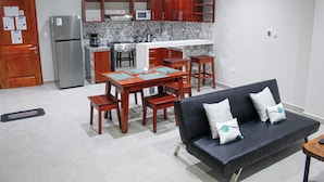A compact kitchen with a refrigerator, stove, and microwave. There is a dining table with chairs and a sofa with cushions. - Bellazio Aparthotel (Iquitos)