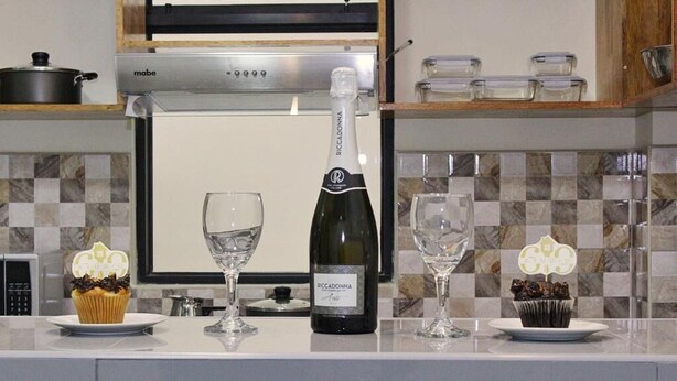 A kitchen counter with a bottle of wine, two glasses, and two cupcakes. - Bellazio Aparthotel (Iquitos)