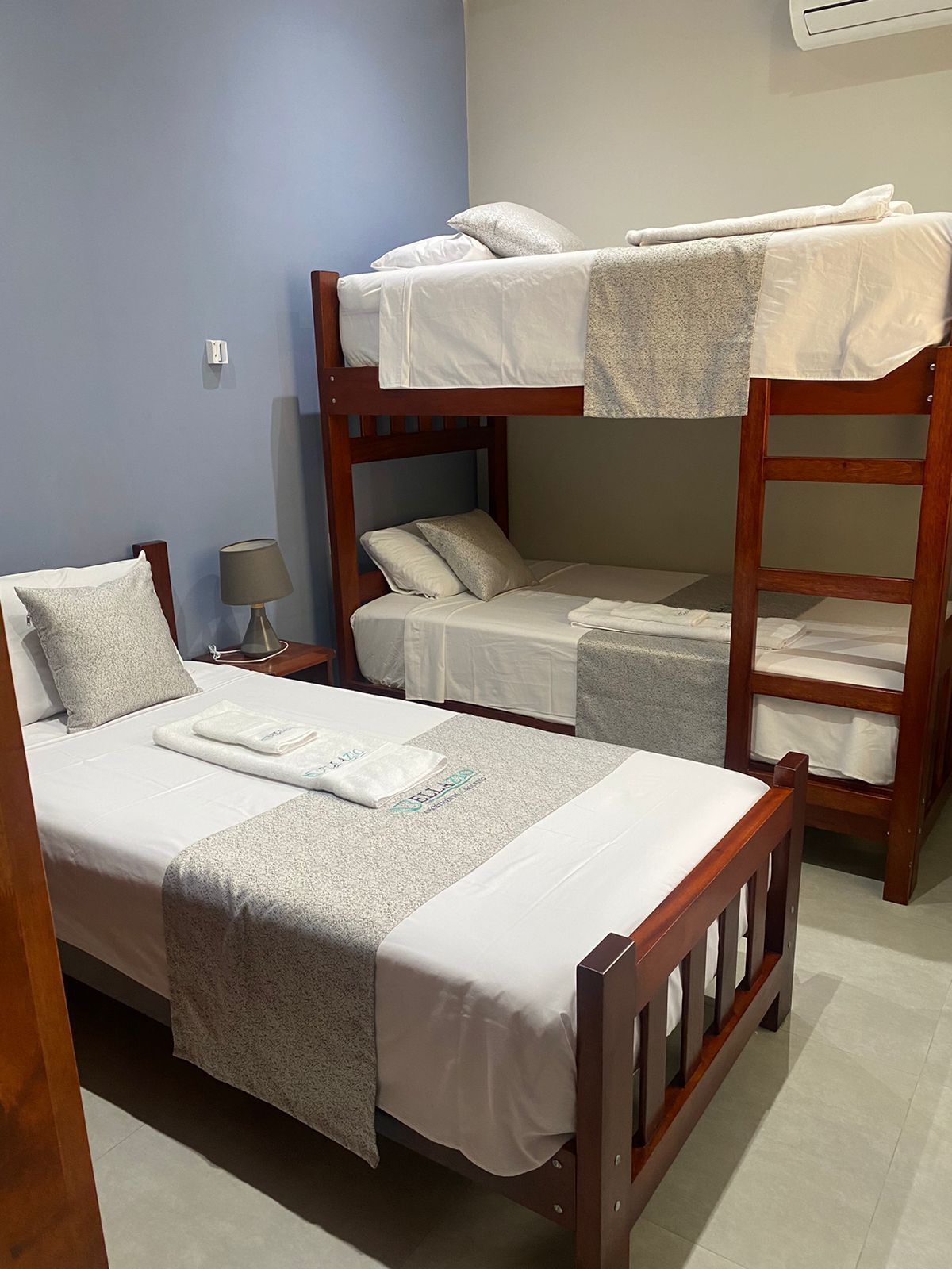 Une chambre avec un lit superposé, deux lits, une table de chevet avec une lampe et un climatiseur fixé au mur.