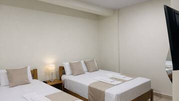 A hotel room with two beds, a bedside table with a lamp, and a TV mounted on the wall.