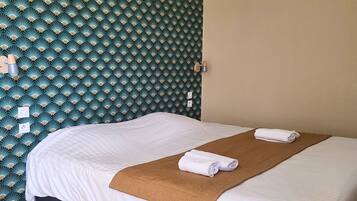 Een keurig opgemaakt bed met witte lakens en een bruine plaid, een houten vloer, en een groene, behangende wand met een gestructureerd plafond.