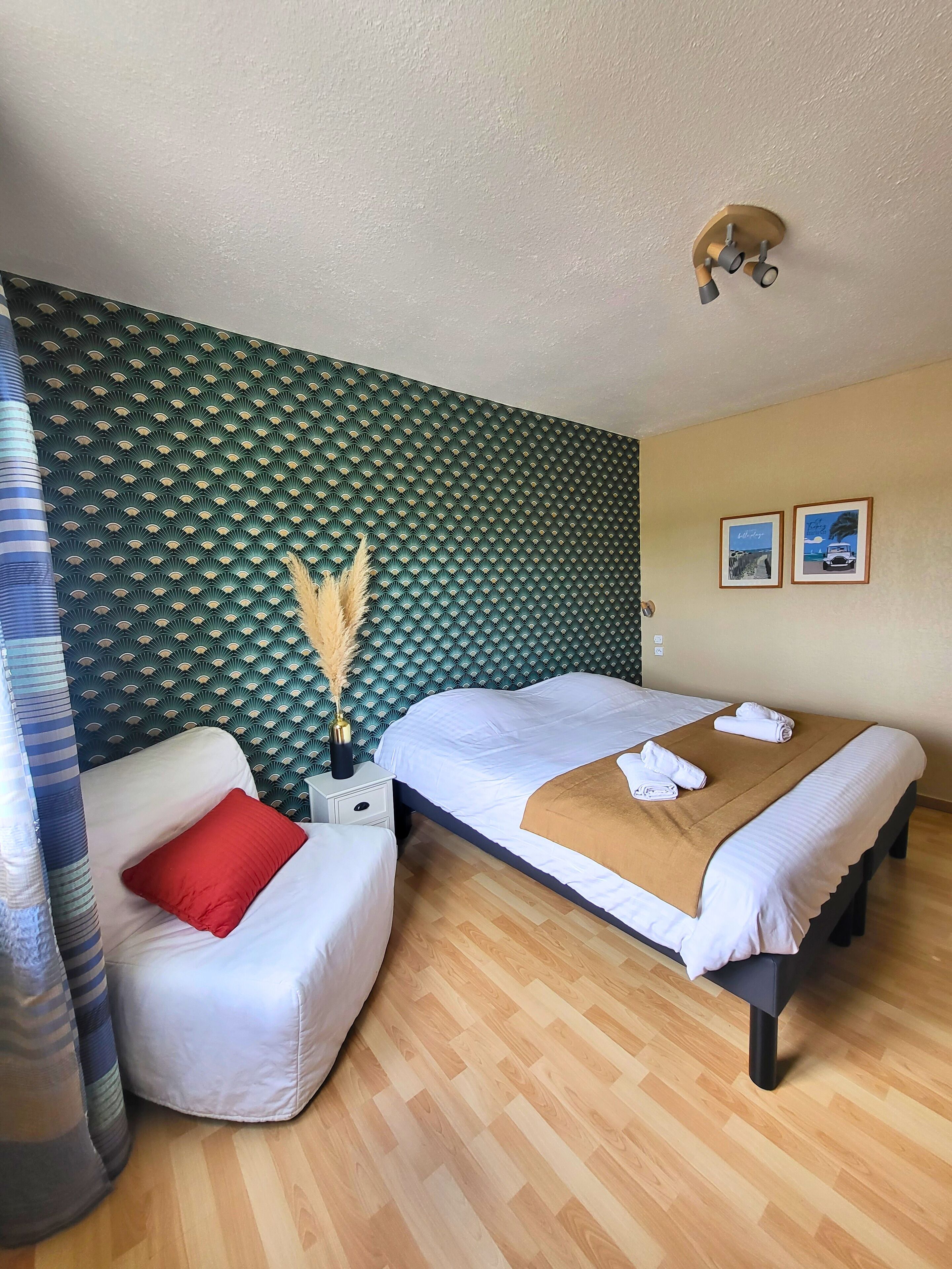 A hotel room with a bed, a small sofa, a nightstand, and a wall with a patterned wallpaper.