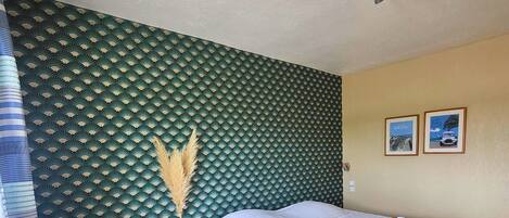 A hotel room with a bed, a small sofa, a nightstand, and a wall with a patterned wallpaper.