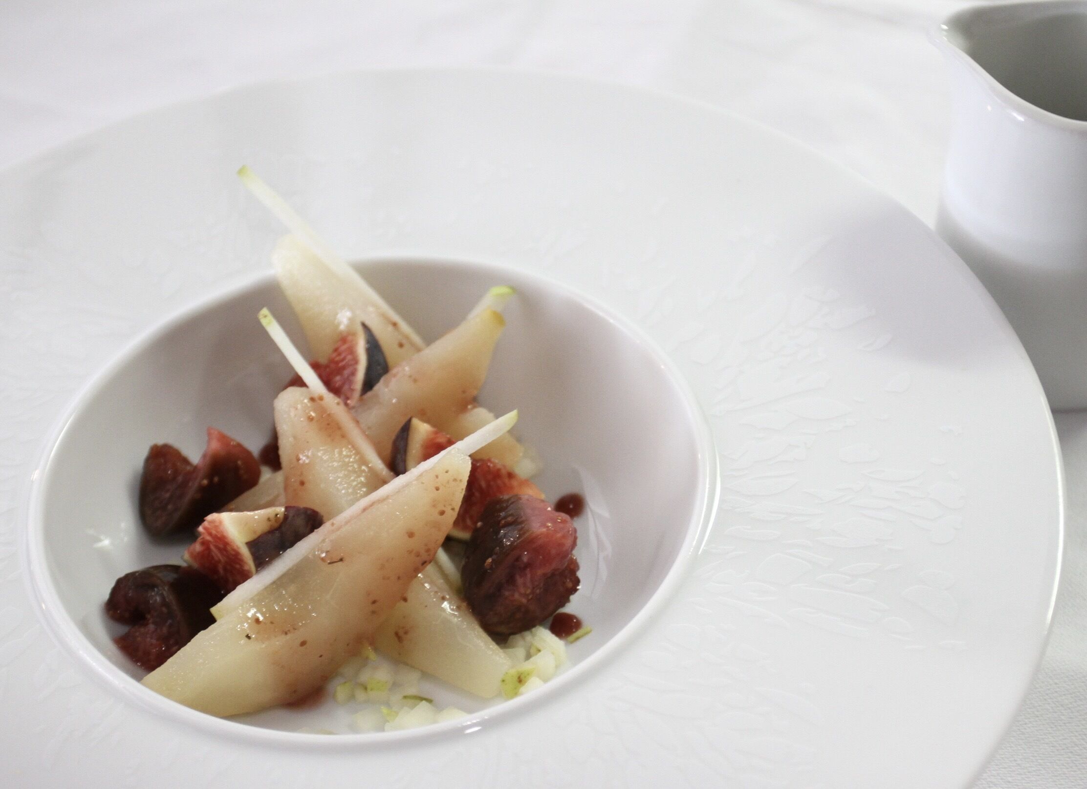 Un plato blanco con un bol pequeño que contiene brochetas de fruta y frutos secos.