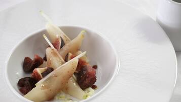 Un plato blanco con un bol pequeño que contiene brochetas de fruta y frutos secos.