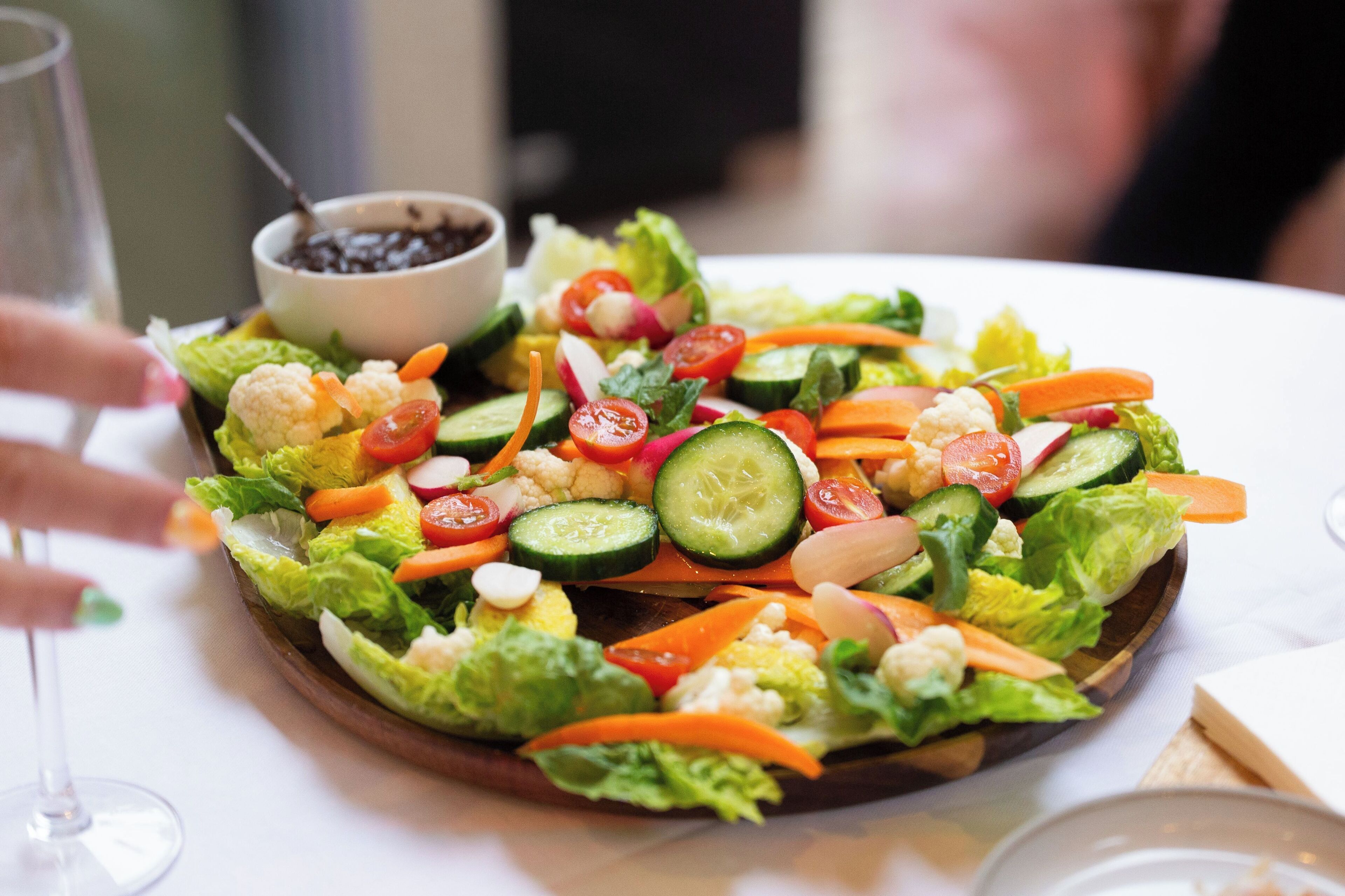 Ensalada con diferentes verduras y un tazón pequeño de frijoles negros sobre un plato de madera.