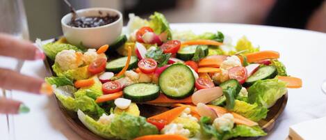 Ensalada con diferentes verduras y un tazón pequeño de frijoles negros sobre un plato de madera.