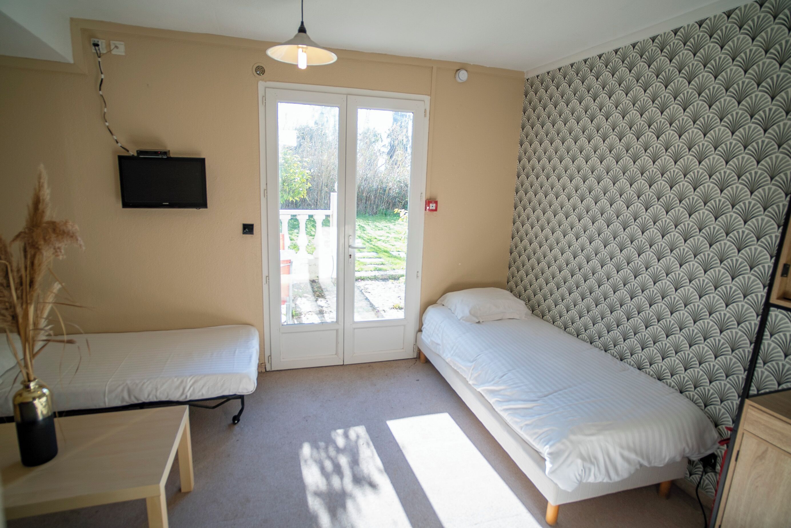 A bedroom with two single beds, a TV mounted on the wall, and a door leading to a balcony.