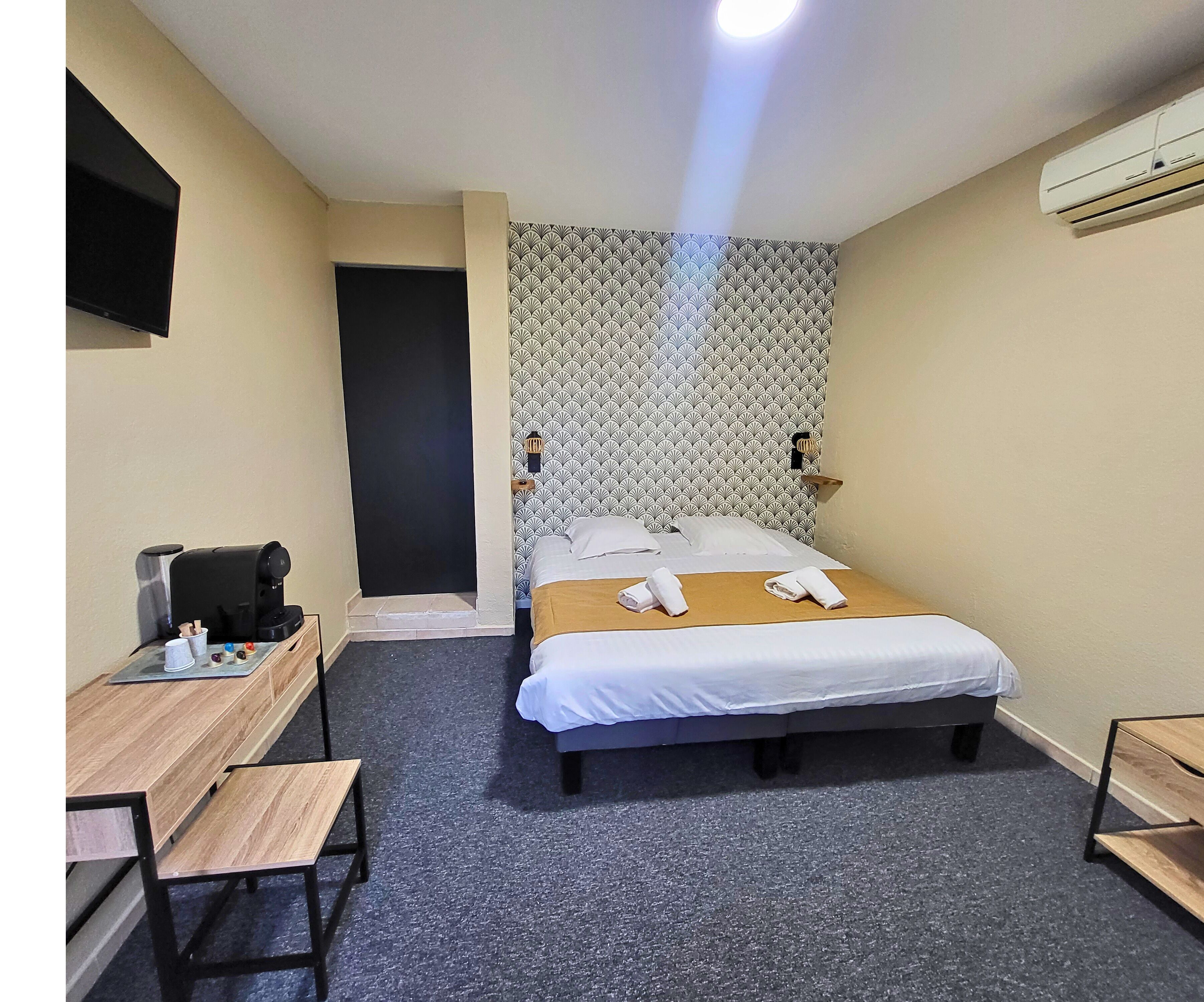 A hotel room with a bed, a desk, a coffee machine, and a wall-mounted TV.