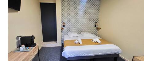 A hotel room with a bed, a desk, a coffee machine, and a wall-mounted TV.