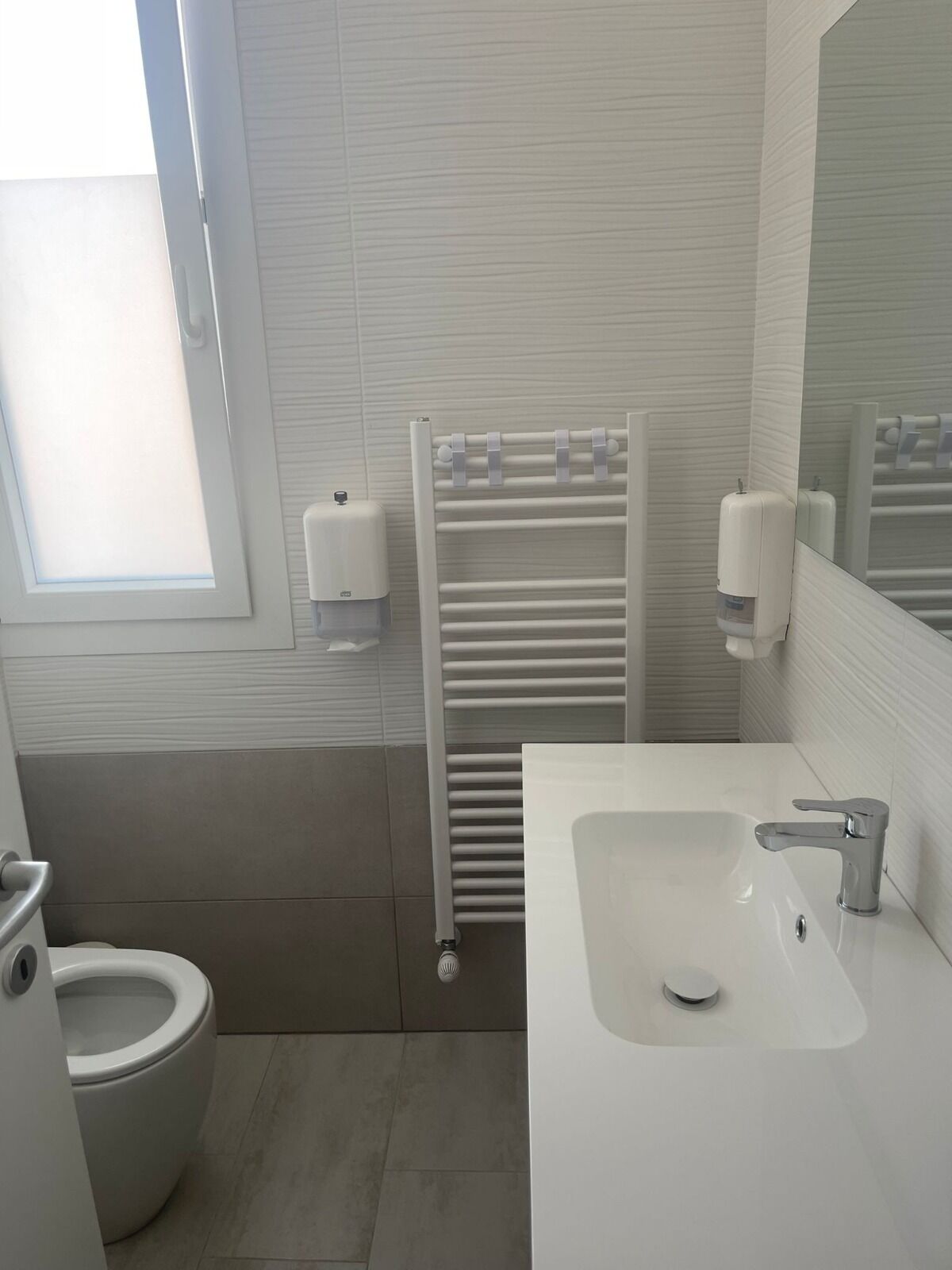 Un bagno moderno con toilette, lavandino, porta asciugamani e finestra.