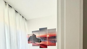 A single bed with a grey mattress and white bedding, a white curtain, and a wall-mounted artwork depicting a sunset over the ocean. - 59 Tourist House Bologna lame (Bologna)
