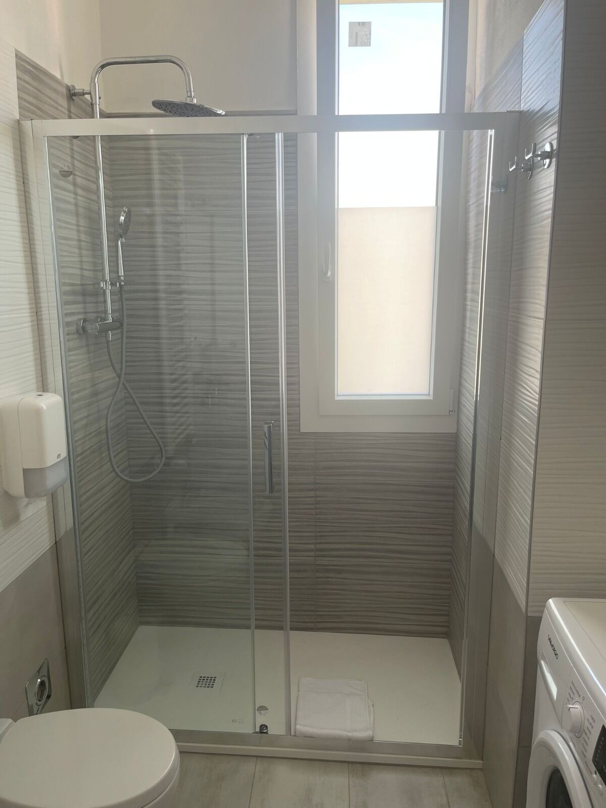 Ein modernes Badezimmer mit einer gläsernen Duschkabine, Toilette und Waschmaschine.