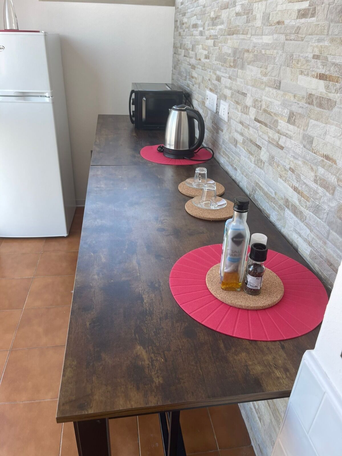 A kitchen with a dark wooden table, a kettle, and two glass bottles on red coasters.