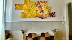 A dining area with a white table and chairs, a large abstract painting on the wall, and an air conditioning unit. - 59 Tourist House Bologna lame (Bologna)