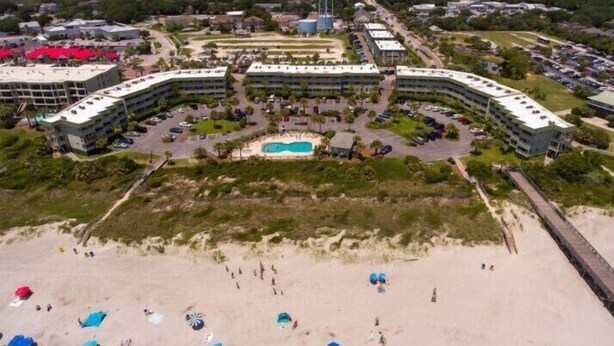 Un hotel costero con varias edificaciones, piscina y zona de playa con sombrillas.
