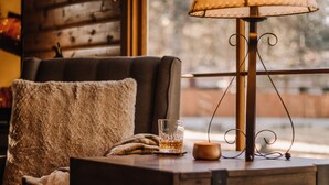 Una sala de estar acogedora con un sofá, una copa de whisky, una lámpara y vistas a través de una ventana.
