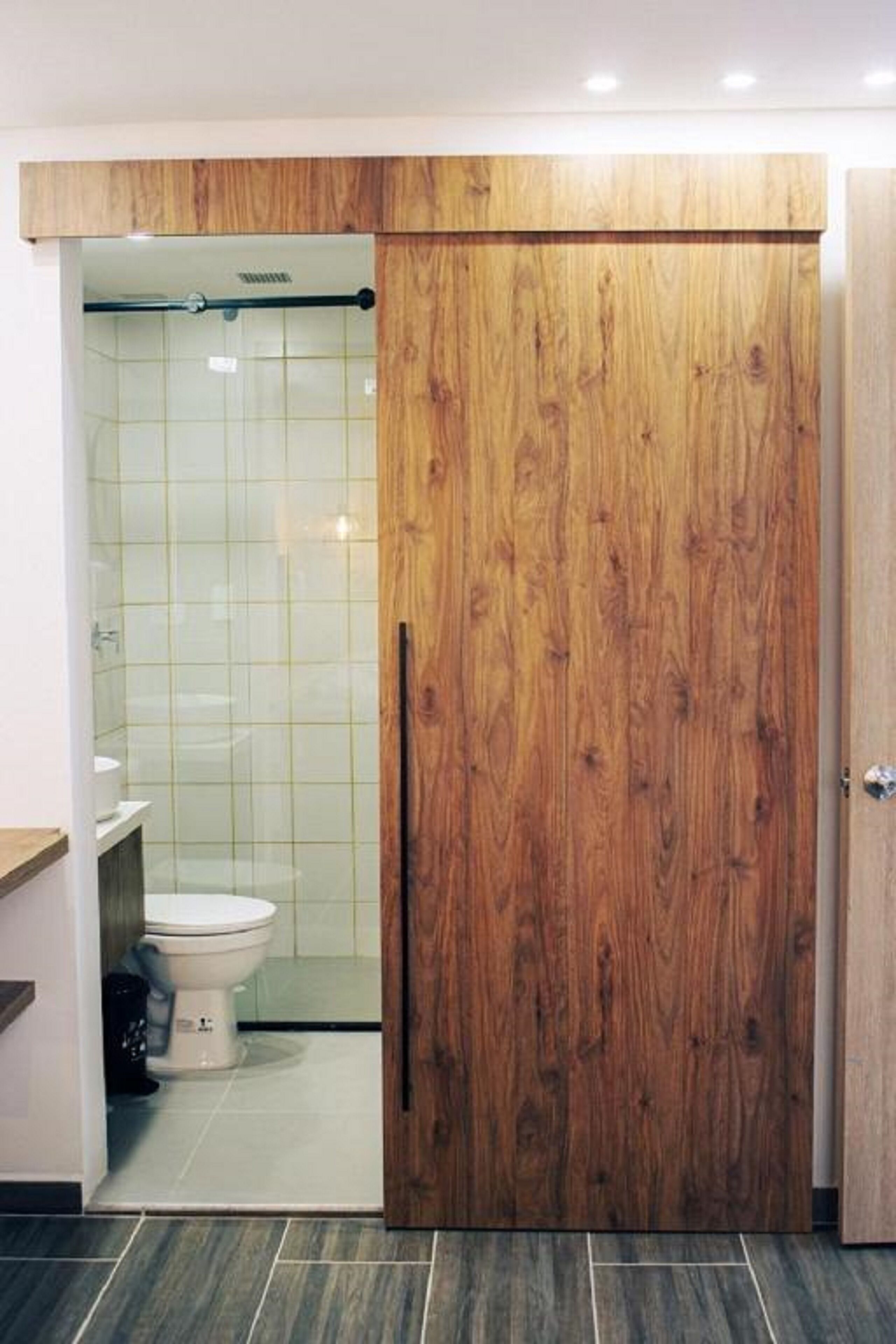 Un baño con puerta de madera, un inodoro y zona de ducha.