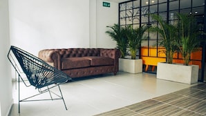 A modern lobby with a brown sofa, a black chair, and potted plants. - Estainn Hotel Coworking (Bogotá)