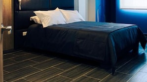 A modern bedroom with a dark-colored bed, a wooden headboard, a pendant light, and a window with a view. - Estainn Hotel Coworking (Bogotá)