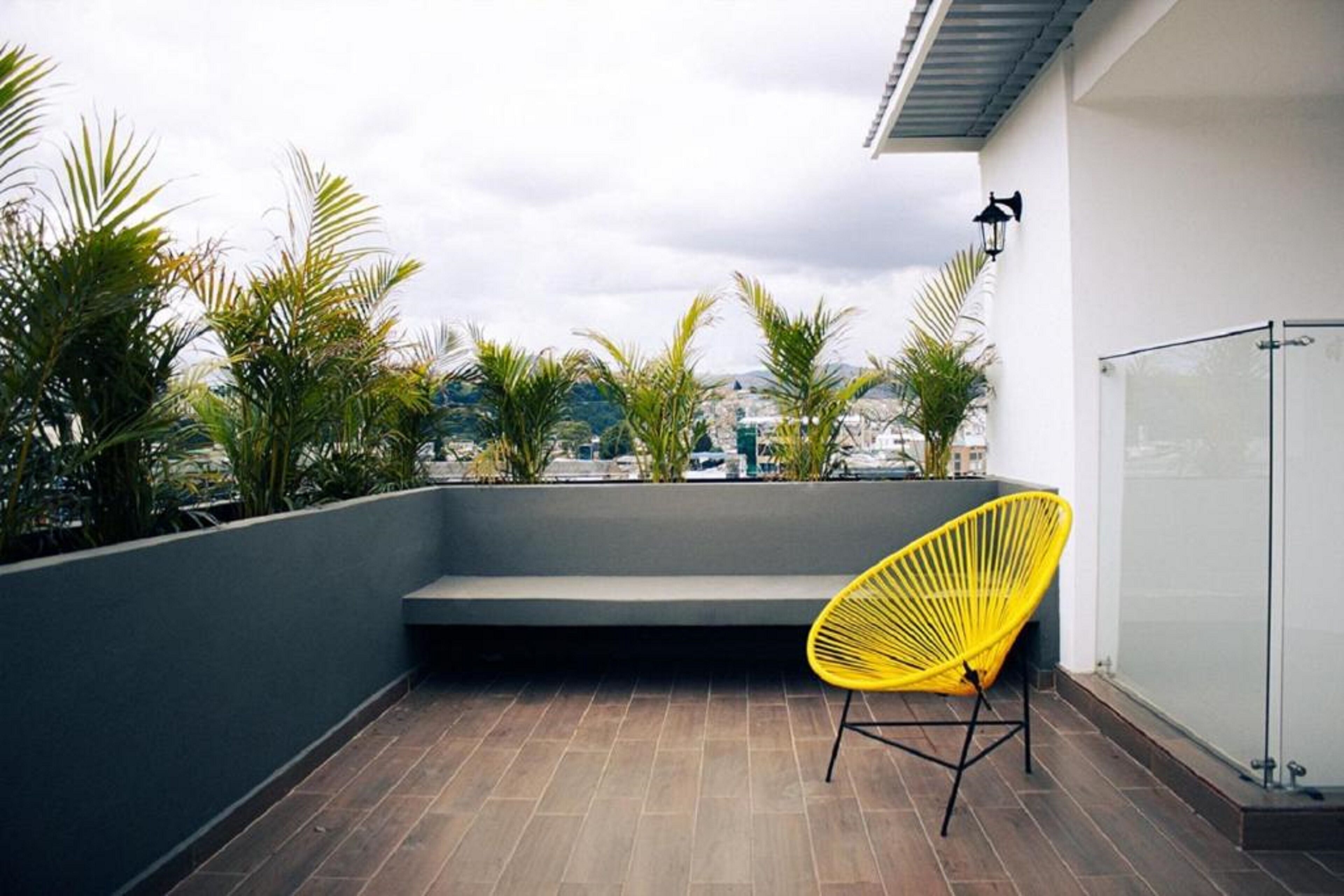 A balcony with a yellow chair, a bench, and a glass door.