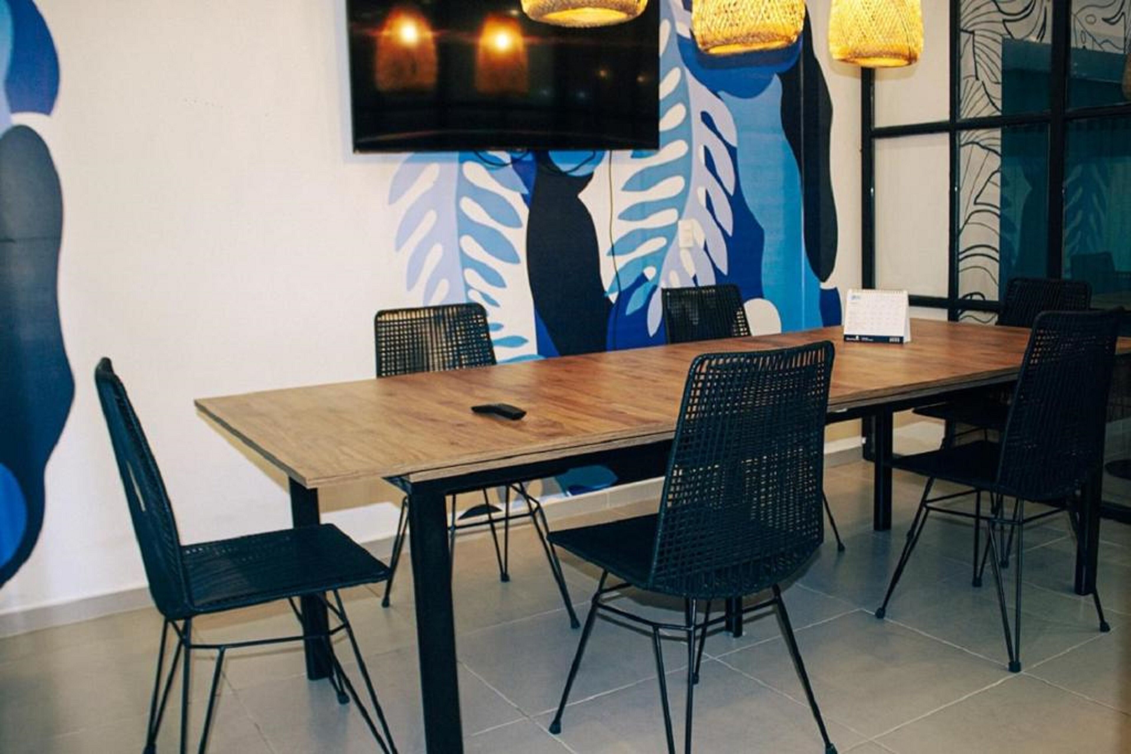 A dining area with a wooden table and black chairs, a flat-screen TV mounted on the wall, and a large abstract mural.