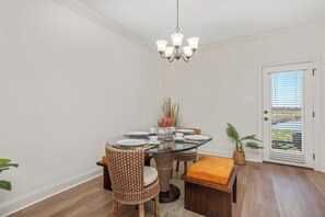 A dining area with a glass table, wicker chairs, a bench, and a chandelier.