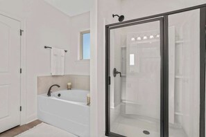 A modern bathroom with a freestanding bathtub, a glass-enclosed shower, and a white tiled wall.