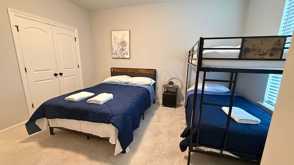 Une chambre avec un lit simple, un lit superposé, une porte, une table de chevet et un tableau accroché au mur.
