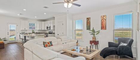 A modern living room with a sectional sofa, a dark armchair, a wooden coffee table, and a ceiling fan.