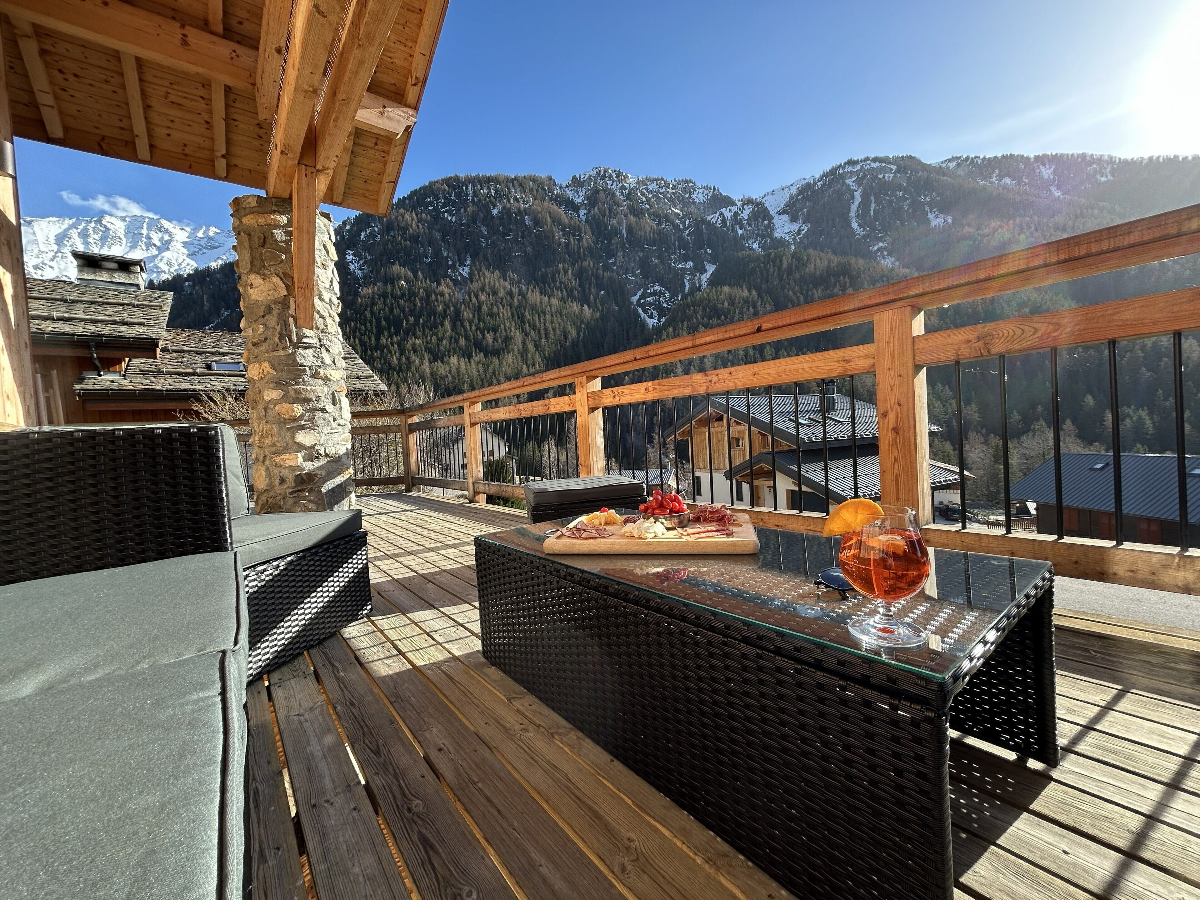 A wooden deck with outdoor furniture, a buffet table with food, and a mountain view.